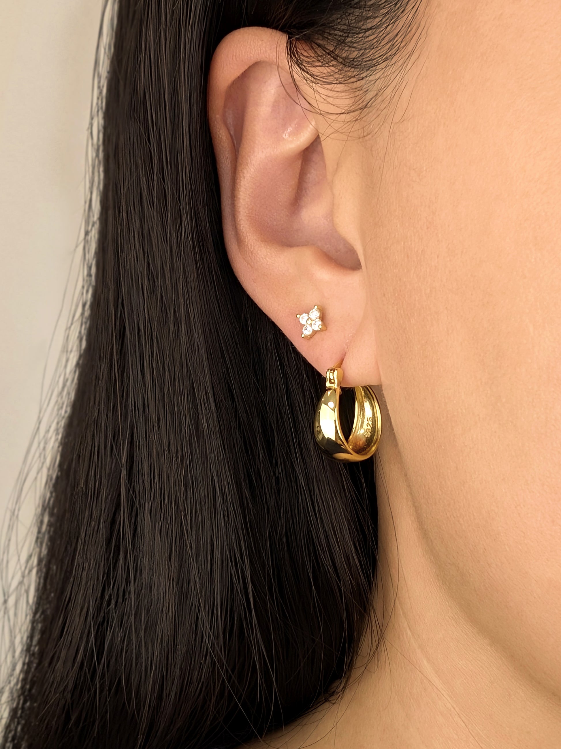 Close-up of FAVES Britt puffed oval hoop earring in 18K gold over sterling silver worn with stud earring.